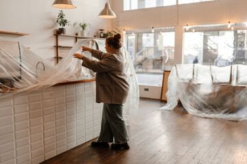 The woman owner stands and removes a bag from the bar in front of her, before the opening of the cafe