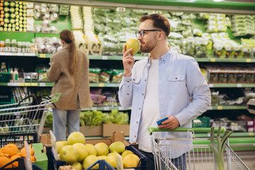 Man smelling an apple while grocery shopping in supermarket