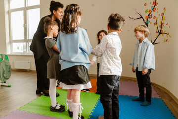 A group of six schoolchildren and a teacher stand in a circle and talk while looking at each other,...