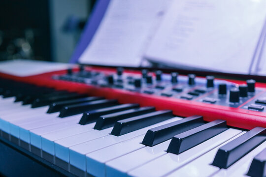 Close-up of digital piano keys and control knobs with a red panel, worship sheet music blurred in the background during church rehearsal