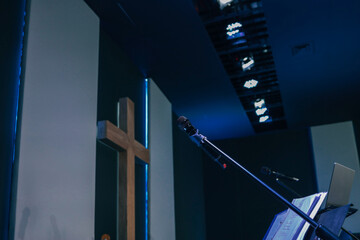 Microphone on a stand with open sheet music and a wooden cross in the background inside a modern...