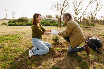 Fototapeta premium A woman and a man are sitting near a plant and holding hands while smiling and looking at each other, outdoors, on a date