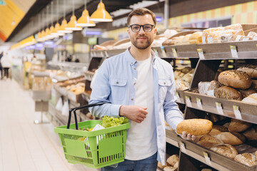 Man Choosing Bread in Supermarket Bakery Section Holding Shopping Basket