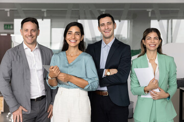 Diverse business team of happy colleagues and Latin female leader standing together in office,...