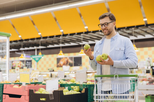 Shopper comparing green apples at produce section, carefully selecting fresh fruit during grocery shopping