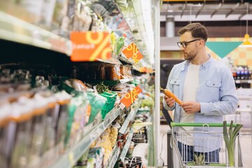 Customer choosing groceries in a supermarket, holding a carrot and looking at the discount prices...