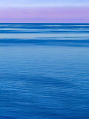 Fototapeta premium Minimalist morning landscape of the calm Aegean Sea under a clear sky. The smooth, deep blue water surface and soft gradients in gentle pastel colours evoke a sense of peacefulness and endless space.