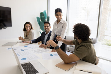 Group of four professionals engaged in collaborative discussion around conference table, reviewing documents, making charts data analysis, smiling, working on presentation. Teamwork and idea-sharing