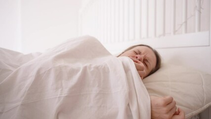 Woman Waking Up in Bright Bedroom Removing Mouth Tape While Yawning and Lying Back Down Under Blanket for Interrupted Sleep Concept