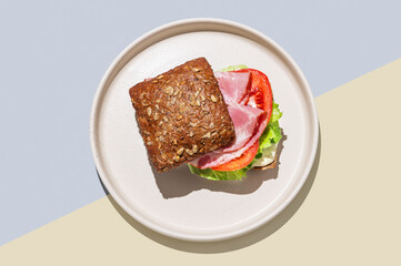 Toast sandwich made of grain bread with prosciutto, tomatoes, lettuce and sauce on blue yellow background