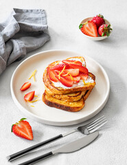 Toasted bread with cream cheese and strawberries on a plate on a light background with fresh berries.