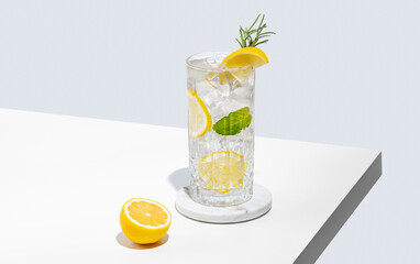 Lemonade with lemon, rosemary and ice in a glass on a white table. Summer citrus drink or mojito cocktail concept