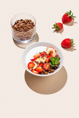 Greek yogurt with chocolate granola, strawberries and banana in a bowl on a yellow background