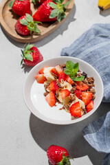 Natural Greek yogurt with homemade chocolate granola, strawberries and banana in a bowl on a light background