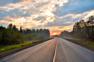 View of the setting sun on the horizon of the highway. Sunset colors reflected on the asphalt road.