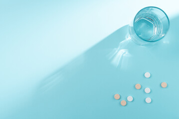 Glass of water and many pills on blue background. Flat lay, top view. Copy space
