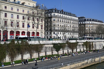Naklejka premium Seine river embankment in Paris with classic Haussmann buildings, bridge, and blue sky. Scenic cityscape of the French capital with historical architecture and calm water.