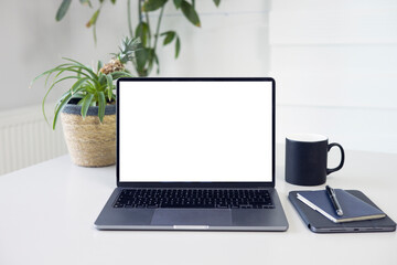 Fototapeta premium Business image, Blank screen computer and supplies. Workspace desk, books, laptop, coffee cup, plant and pen. Laptop mock up screen view. Work from home concept 