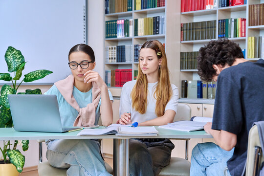 Group of students teenagers sitting together at desk in library preparing for tests exams - Powered by Adobe