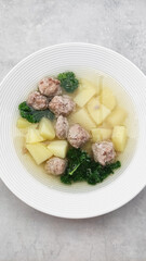 Wedding soup with meatballs, potatoes and parsley is steaming in a white bowl