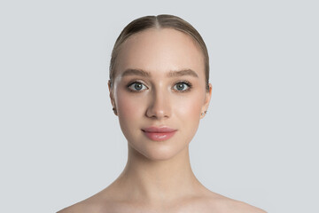 Face of attractive fair-haired girl on white background. Head of woman in full face, face close-up. Concept of face care, skin moisturizing, beauty and youth