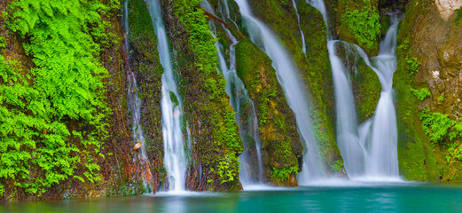 small waterfall on emerald mountain river rushing over a green stones