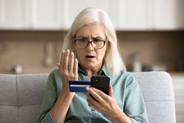 Financial loss fear. Nervous worried senior lady hold credit card look at phone screen unable to...