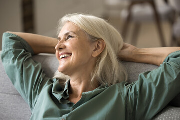 Optimistic aging. Close up portrait happy content senior adult lady retiree sit on comfy couch in...