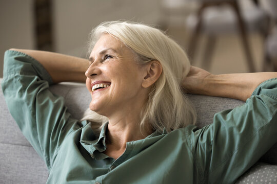 Optimistic aging. Close up portrait happy content senior adult lady retiree sit on comfy couch in relaxed pose looking aside with serene smile enjoy home comfort peace of mind feel satisfied with life