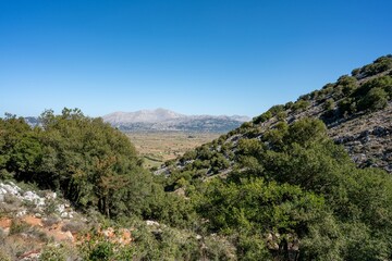 A stunning view of Greece’s rural landscape featuring lush green hills, rocky outcrops, and...