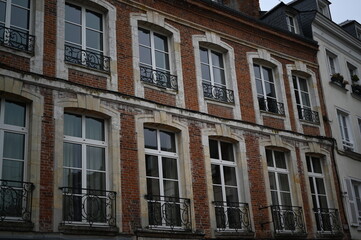 classic French brick façade with tall white-framed windows and elegant wrought-iron balconies. Historic European architecture under an overcast sky, creating a timeless and authentic urban atmosphere.