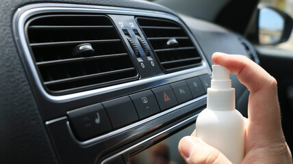 Hand spraying air freshener in car interior ventilation system