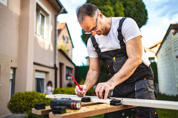 Mature male carpenter measuring wooden plank outdoors
