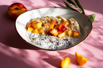 Chia pudding bowl with yogurt and fruit. Yogurt with chia seeds, banana and peach on a pink background.