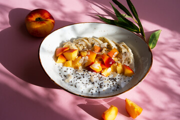 Chia pudding bowl with yogurt and fruit. Yogurt with chia seeds, banana and peach on a pink background.