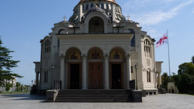 Poti Soboro Ortthodox Christian Cathedral gleaming against blue sky, golden dome rising, national flag of Georgia waving proudly over architectural landmark