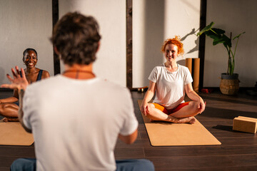 A yoga instructor guiding a student in a yoga studio with large windows and wooden floors.