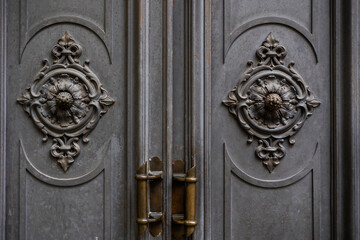 Detailed view of an ornate metal door featuring floral and geometric motifs in a classical style, with brass handles.