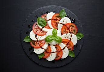 High resolution image of a classic Caprese salad layered mozzarella, basil, and tomatoes with balsamic drizzle styled on slate, perfectly centered on a rich black backdrop.