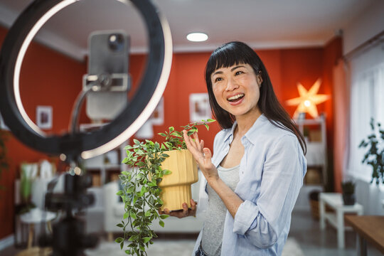 Japanese woman use mobile phone for live stream about home plants - Powered by Adobe