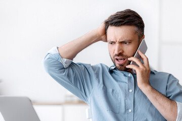 Frustrated businessman having problems with computer in office, talking on cellphone with customer...
