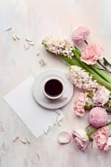 Flat lay with morning cup of coffee, empty card and bouquet of flowers on pastel concrete background. Top view, copy space