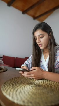 A young woman is engaged with her smartphone while comfortably sitting at home in a relaxed setting