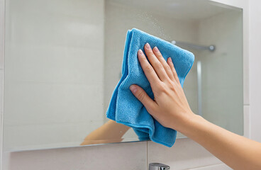 Caucasian woman s hand cleaning mirror with microfiber cloth in modern bathroom. concept of home care, cleaning routine, and hygiene maintenance