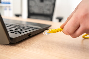 Close up of woman hands plugging ethernet cable on laptop on a desktop