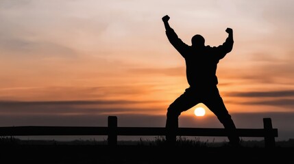 Fototapeta premium Silhouette of triumphant young adult male at sunset against scenic horizon