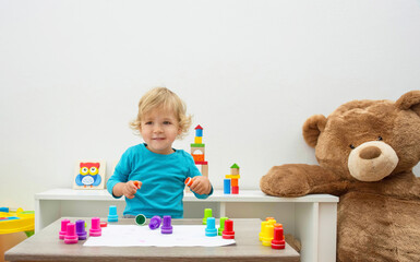 Cute little child boy having fun at home playing with colorful stamps on paper. Educational indoor activity for kids.