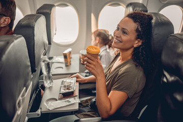 A woman delights in a delicious meal and drink on her flight, enhancing her unforgettable travel...