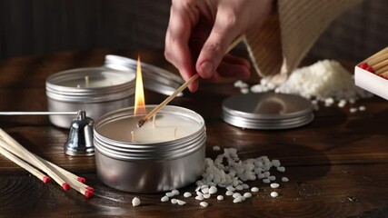 Woman lighting soy wax candle with long match at wooden table, closeup
