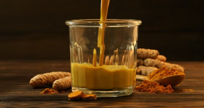 Pouring delicious turmeric latte into glass at wooden table, closeup